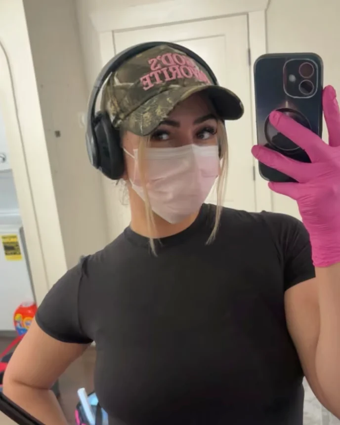 Jenny on a job, in a cap, headphones, a mask and pink cleaning gloves.