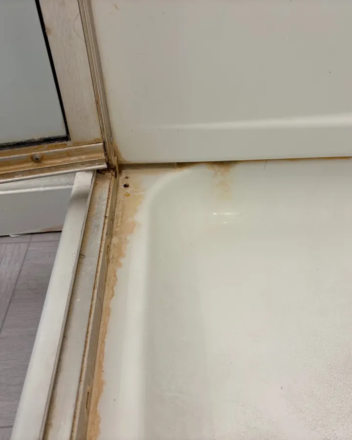 Before: orange buildup along a shower door track.