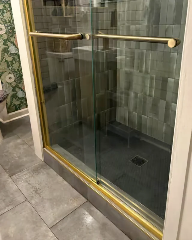 After: the same shower door clear, with the brass handle and track polished.