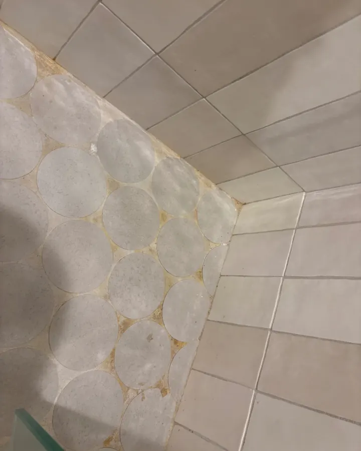 Before: shower floor tile with orange buildup in the grout lines.