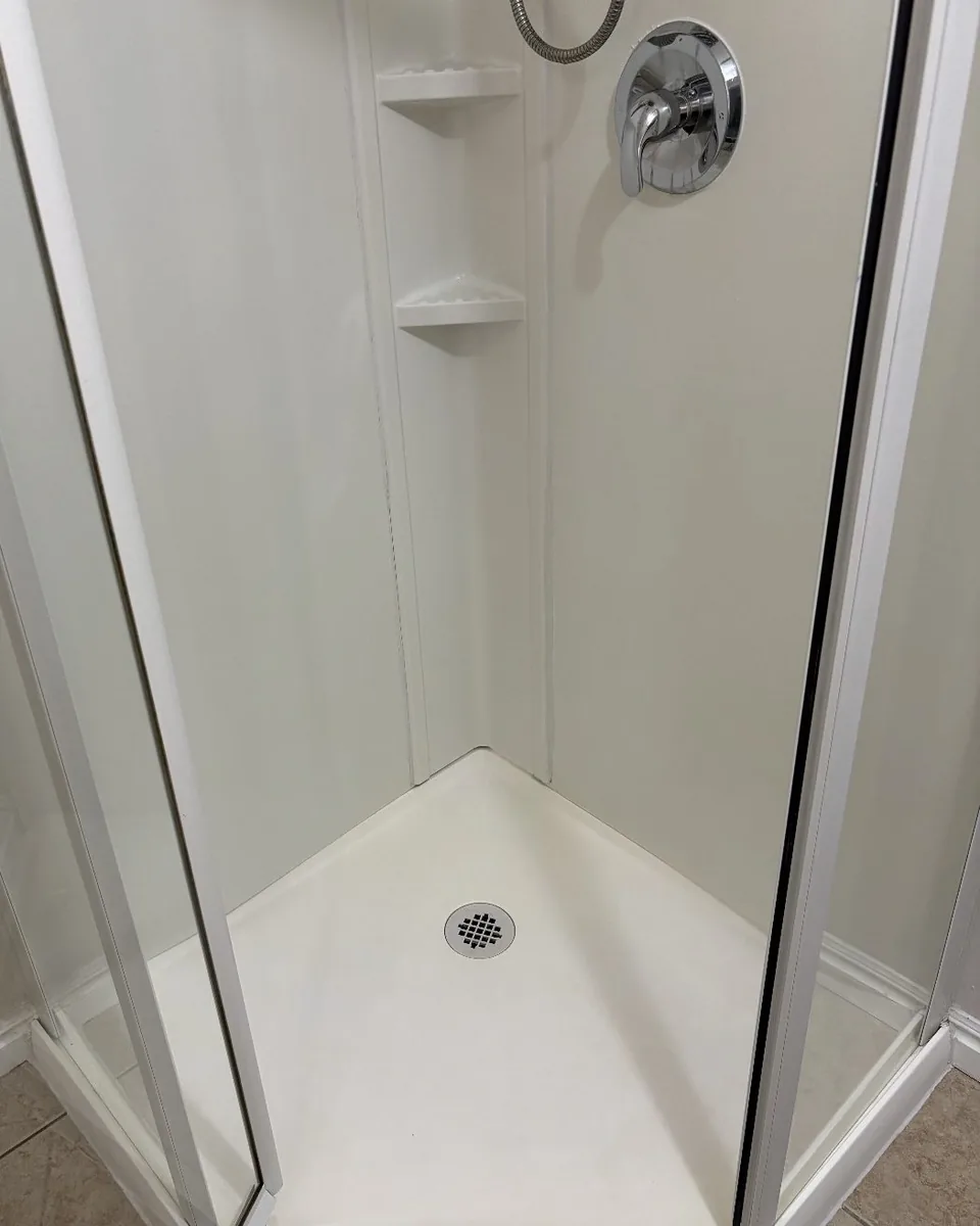 After: the same corner shower with a bright white floor and clear glass.