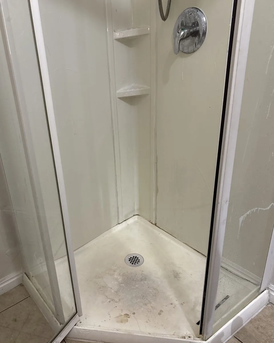 Before: a corner shower with a grimy, stained floor and streaked glass.