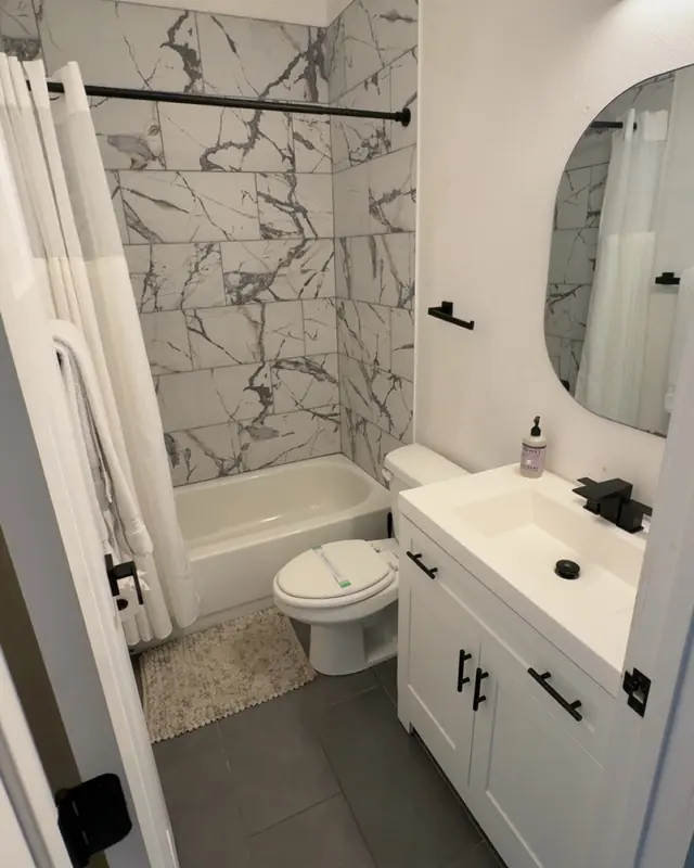 A guest bathroom with marble-look tile, a clean tub and a white vanity.
