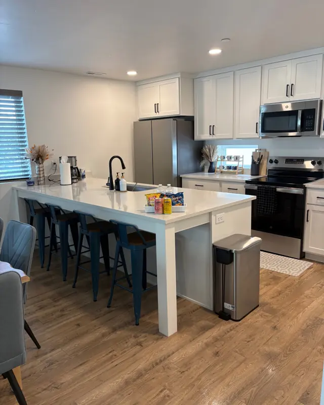 A white kitchen with a long island, bar stools and clear counters.