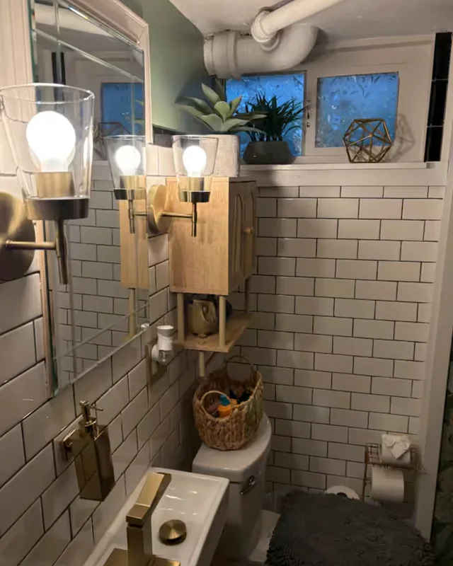 A small bathroom with white subway tile, brass sconces and tap, and a polished mirror.