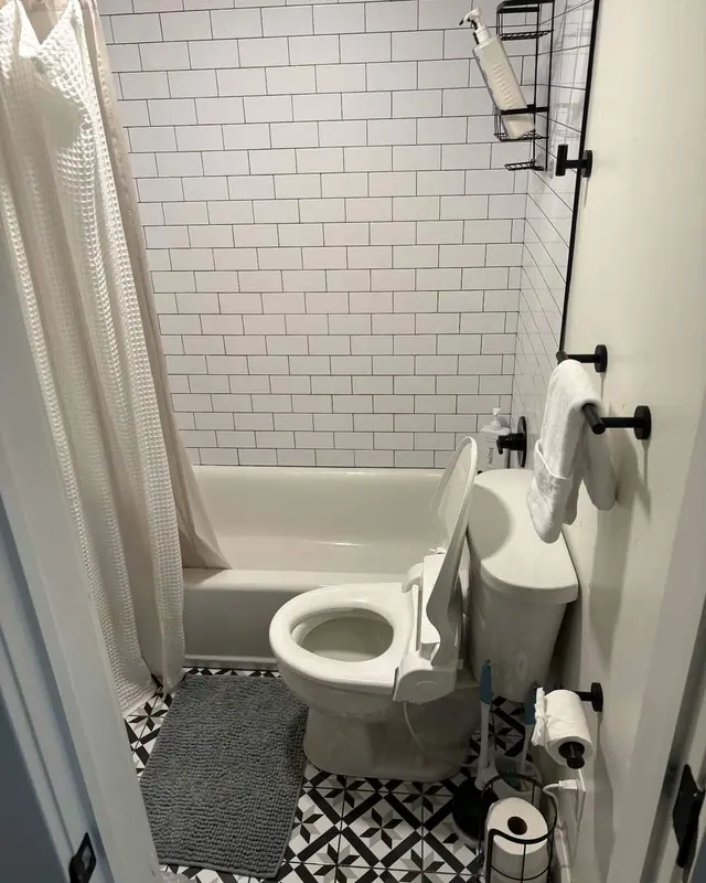 A bathroom with white subway tile, a clean tub and a patterned floor.