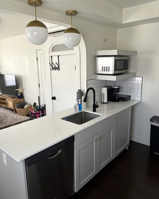 A small kitchen with grey cabinets, globe pendant lights and clear white counters.
